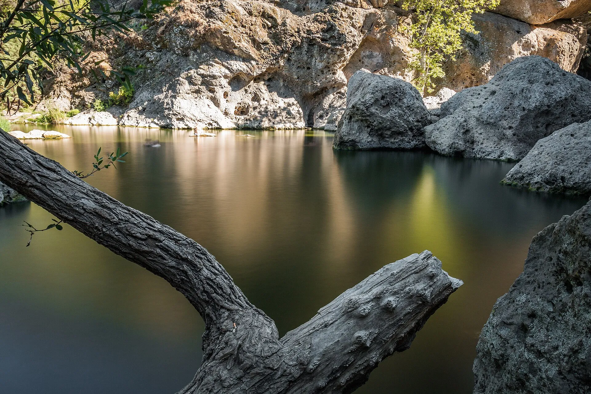 Still green water of the Rock Pool beneath pocketed volcanic cliffs at Malibu Creek