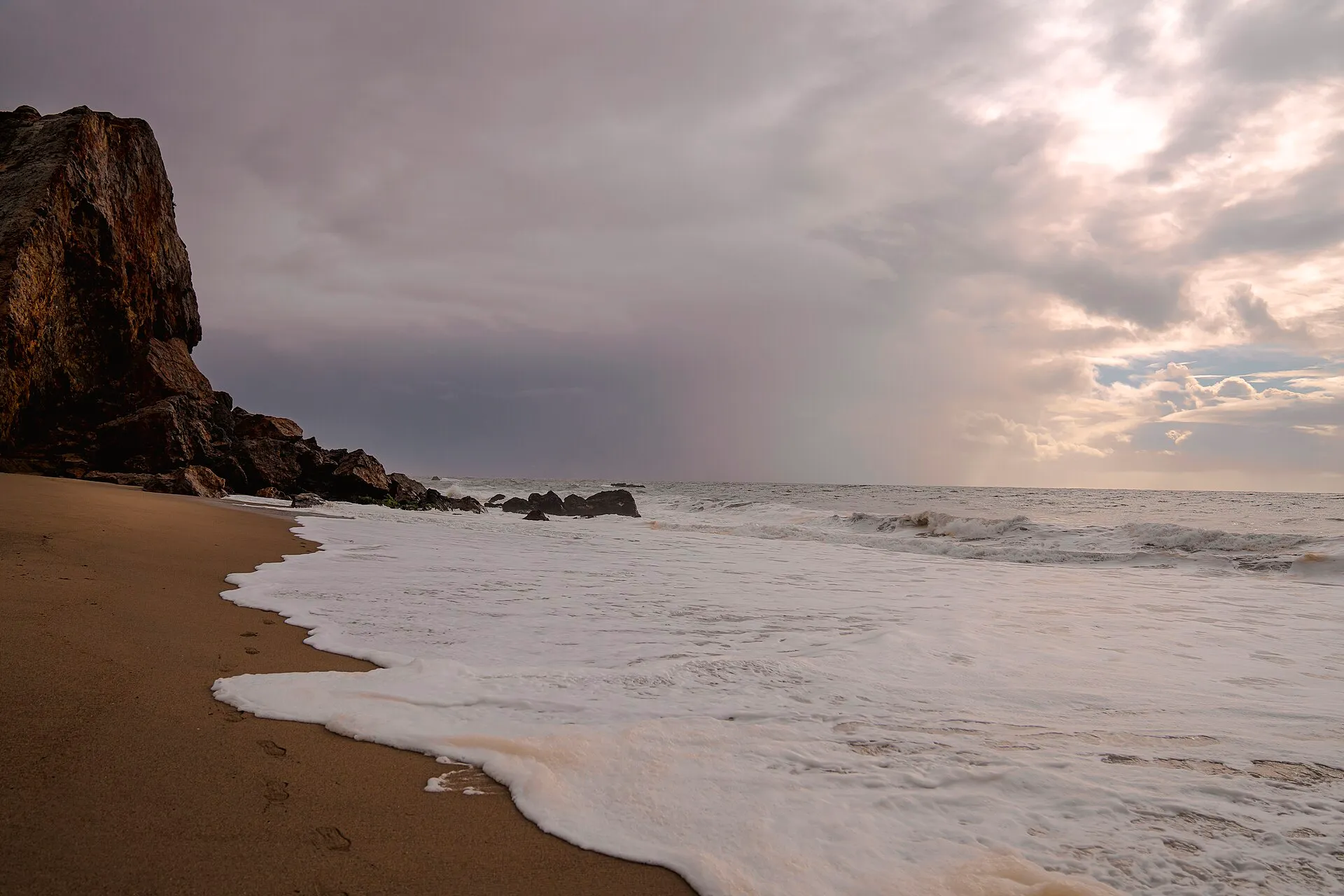 The dark Point Dume headland above the surf under dramatic clouds