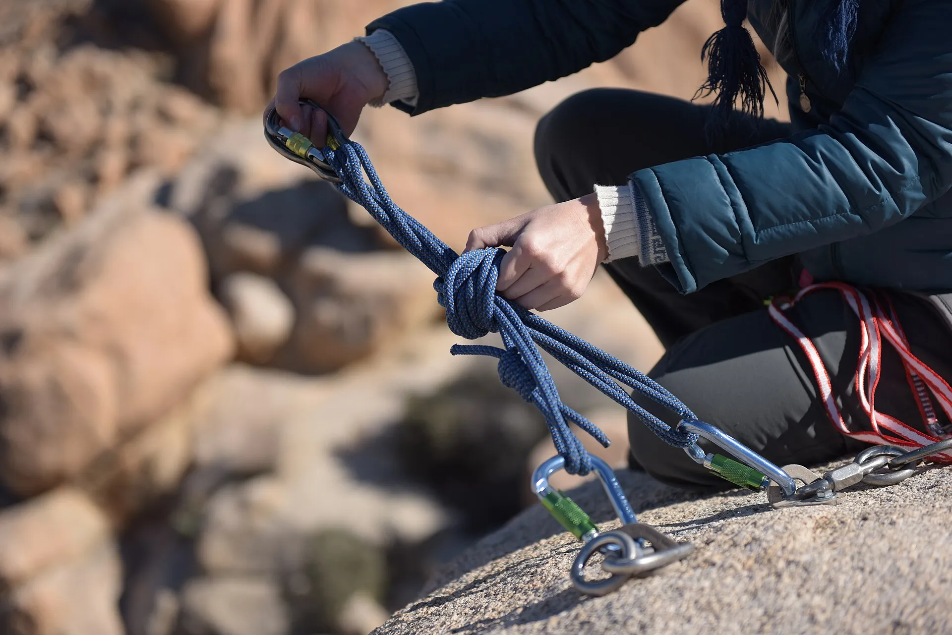 Hands threading a rope through carabiners on a bolted anchor